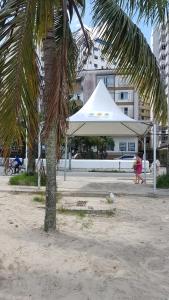 a white tent on a beach with a palm tree at Pé na areia Gonzaguinha São Vicente in São Vicente