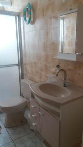 La salle de bains est pourvue d'un lavabo, de toilettes et d'un miroir. dans l'établissement Apartamento na avenida da praia, à Praia Grande
