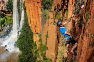 een man die aan het rotsklimmen is op een klif naast een waterval bij Climber's house in Waterval Boven