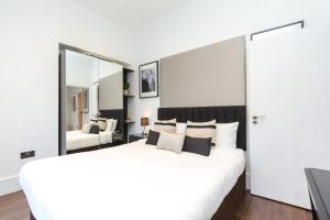 a bedroom with a large white bed and a mirror at Clockwork London Flats in London