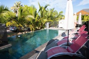 a swimming pool with chairs and an umbrella and palm trees at Canne Mapou1 in Saint-Pierre