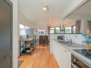 a kitchen with white cabinets and a wooden floor at Beach House on Hetherington - Whangamata Home in Whangamata