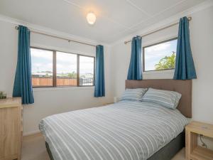 a bedroom with a bed and two windows with blue curtains at Beach House on Hetherington - Whangamata Home in Whangamata