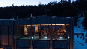 a glass house with a dining room in it at night at Olangerhof Hotel & Spa in Valdaora