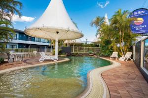 a pool with an umbrella and chairs in a resort at Comfort Inn All Seasons in Ballina