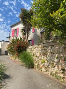 eine Steinmauer neben einem Haus mit rosa Fensterläden in der Unterkunft Gîte Orloucie au coeur des Abers proche de tout in Lannilis