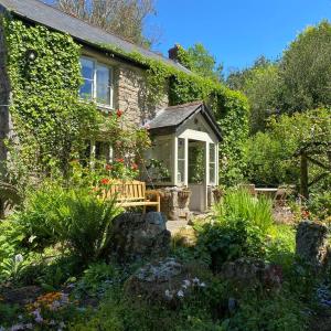 uma casa de pedra com um banco num jardim em Dog friendly cottage with woodland & lake em Helston