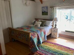 um quarto com uma cama com um cobertor colorido e uma janela em Dog friendly cottage with woodland & lake em Helston