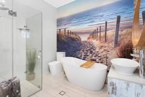 a bathroom with a bath tub and a painting of a beach at Driftwood Beach House in Kiama