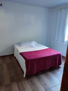 1 dormitorio con 1 cama blanca con manta morada en Casa Silvano's II, en Foz do Iguaçu