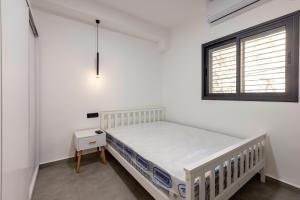 a white bedroom with a bed and a window at Boutique Central old town Apartment in Beer Sheva