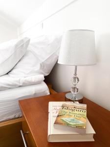 a lamp on a table next to a bed with a book at Fado Apartments Lendava in Lendava