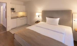 a bedroom with a large white bed and a kitchen at VI VADI HOTEL downtown munich in Munich
