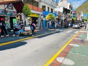 una calle con gente sentada en un banco a un lado de la carretera en Hermoso apartamento en Baños de Agua Santa, en Baños