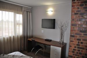 a room with a desk and a television on a wall at Merchant Business Class Hotel in Henley on Klip