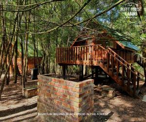 uma ponte de madeira sobre uma parede de tijolos ao lado de uma cabana em Plett Forest Cabins em Plettenberg Bay