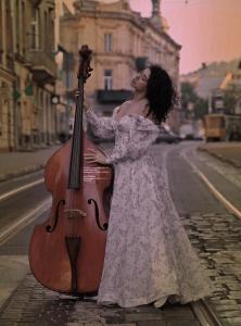 Una mujer con un vestido blanco sosteniendo un violonchelo en Apart-Hotel City Center Contrabas, en Leópolis