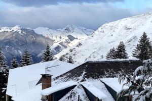 uma casa coberta de neve com montanhas ao fundo em Appartement cocooning 2 chambres em Gourette