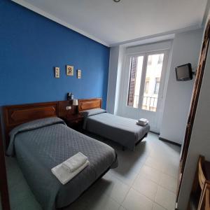 Habitación azul con 2 camas y ventana en Hostal Pan America, en Madrid
