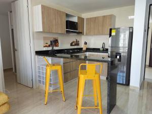 cocina con 2 taburetes amarillos y nevera en Apartamento en Hacienda Peñalisa Ceiba, Sol, Piscina y descanso, en Girardot