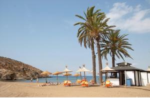 a beach with palm trees and chairs and umbrellas at Agradable casa con piscina in Bolnuevo