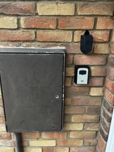 uma caixa preta numa parede de tijolos com uma lata de lixo em Victoria Gardens em Colchester