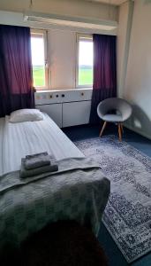a bedroom with a bed and a chair and two windows at Hotell Tre Systrar in Eskilstuna