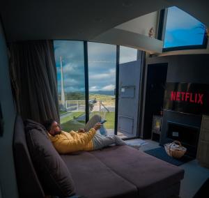 a man laying on a couch reading a book at Tiny House Cambará in Cambará