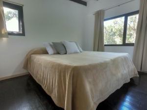 1 dormitorio con 1 cama con colcha blanca y 2 ventanas en Cabaña de mar en Quequén