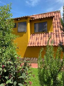 una casa amarilla con techo rojo y algunos arbustos en Cabaña Villa Makus, en Paipa