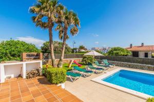 a backyard with a swimming pool and chairs and a palm tree at Villa Tuduri in Binibeca
