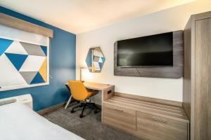 Holiday Inn Express & Suites Phoenix - Mesa West, an IHG Hotel في ميسا: غرفة في الفندق بها مكتب وتلفزيون على جدار