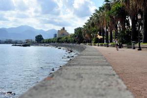 a person walking along a sidewalk next to a body of water at Home Square in Milazzo