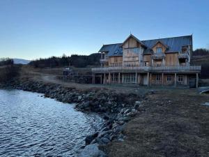 a large wooden house next to a body of water at Amazing and secluded northern light apartment near sea and city! in Selnes