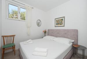 a white bedroom with a bed and a chair at Apartments by the sea Seget Vranjica, Trogir - 1037 in Seget Vranjica