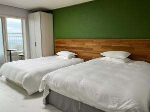 two beds in a bedroom with a green wall at Hill Hotel in Jeju