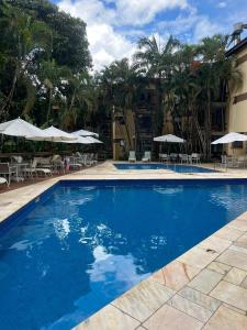 a large blue swimming pool with chairs and umbrellas at Apto Riviera de São Lourenço com Piscinas Aquecidas,Quadra,Sacada Gourmet in Bertioga
