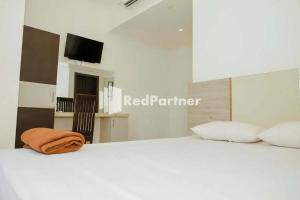 Una cama blanca con una manta naranja encima. en Radja Homestay Mitra RedDoorz, en Pipulu