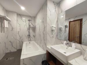 bagno con lavandino, vasca e specchio di UNHAS HOTEL & CONVENTION a Patjinongong