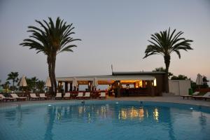 a swimming pool with palm trees and a restaurant at Adams Beach Hotel & Spa in Ayia Napa