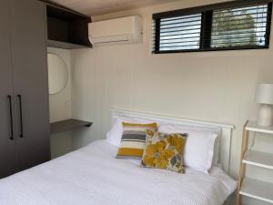una camera da letto con un letto bianco con cuscini e una finestra di Pukeko Lane a Tauranga