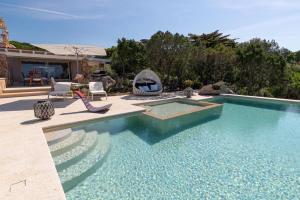 una piscina in un cortile con sedie e una casa di VILLA AMIRA Porto Cervo con vista Mozzafiato sul Mare,Piscina Privata,WELLNESS & SPA a Liscia di Vacca
