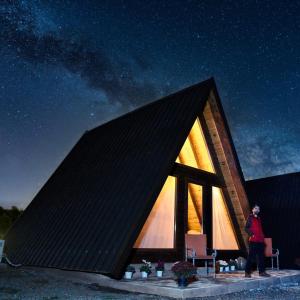 a man standing in front of a triangular house at night at Agora Farmhouse in Koman