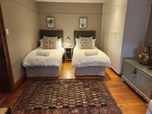 a bedroom with two beds and a rug at Wishford Cottage on Worcester in Grahamstown