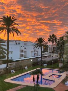 einen Sonnenuntergang über einem Pool mit Palmen und Gebäuden in der Unterkunft Piso Los Angeles - 1ra Linea de Playa in Denia