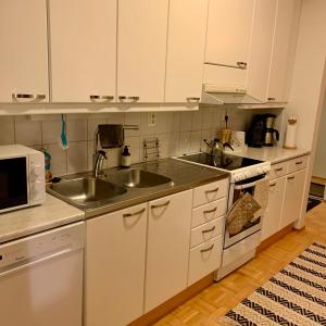 a kitchen with white cabinets and a sink and a microwave at Spacious Apartment close to the sea with 2 patios in Pietarsaari