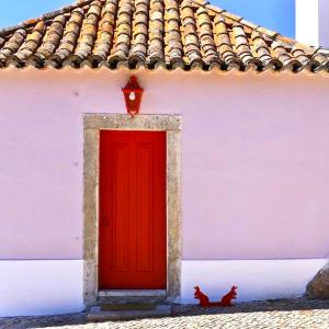 une porte rouge et un chat assis devant un bâtiment dans l'établissement Quinta da Arrábida, à Sesimbra
