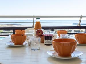a table with plates and cups and a bottle of orange juice at Apartment Le Sunset-Cap Sud-12 by Interhome in Cap d'Agde