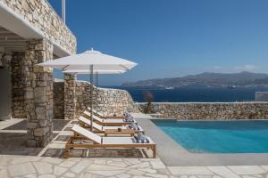 un gruppo di sedie a sdraio e un ombrellone accanto alla piscina di Mykonos Esti Luxury Villas ad Agios Ioannis