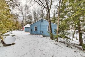 una casa azul en la nieve junto a los árboles en Palmyra Cottage with Deck on Whites Pond!, en Coburn